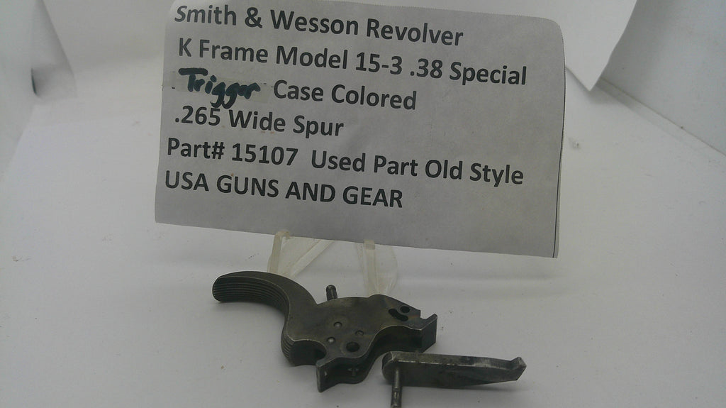 A used Smith & Wesson revolver trigger component on a clear plastic stand in front of a paper label card with product details.