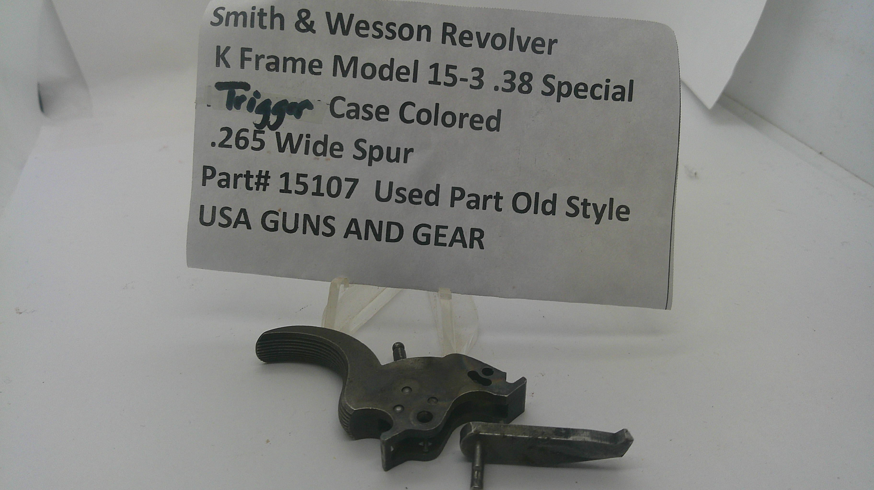 A used Smith & Wesson revolver trigger component on a clear plastic stand in front of a paper label card with product details.