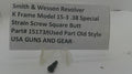 A small black metal strain screw shown on a white surface with a handwritten label card reading 'Smith & Wesson Revolver K Frame Model 15-3 .38 Special Strain Screw Square Butt Part# 15173 Used Part Old Style USA GUNS AND GEAR'.