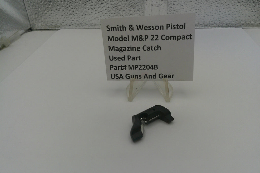 Smith & Wesson pistol magazine catch on a white surface with a label
