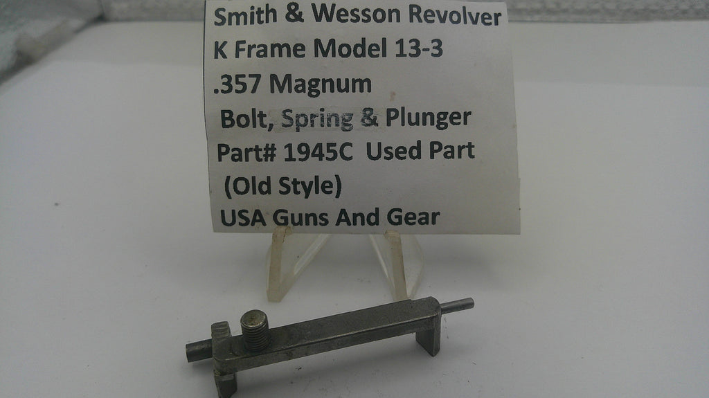 A small metal used part for a Smith & Wesson revolver, displayed on a clear plastic stand with a white label card. The label reads 'Smith & Wesson Revolver K Frame Model 13-3 .