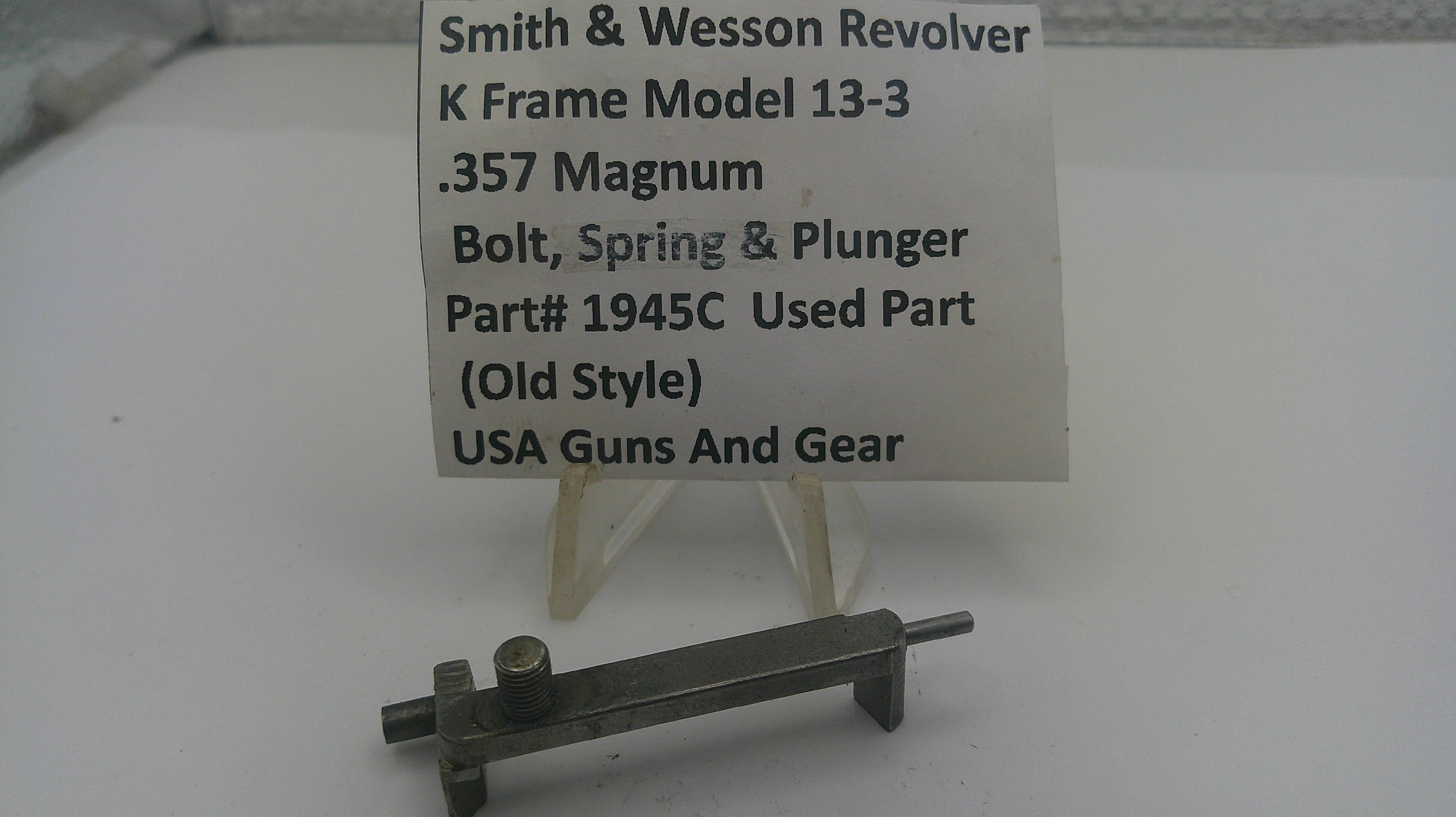 A small metal used part for a Smith & Wesson revolver, displayed on a clear plastic stand with a white label card. The label reads 'Smith & Wesson Revolver K Frame Model 13-3 .