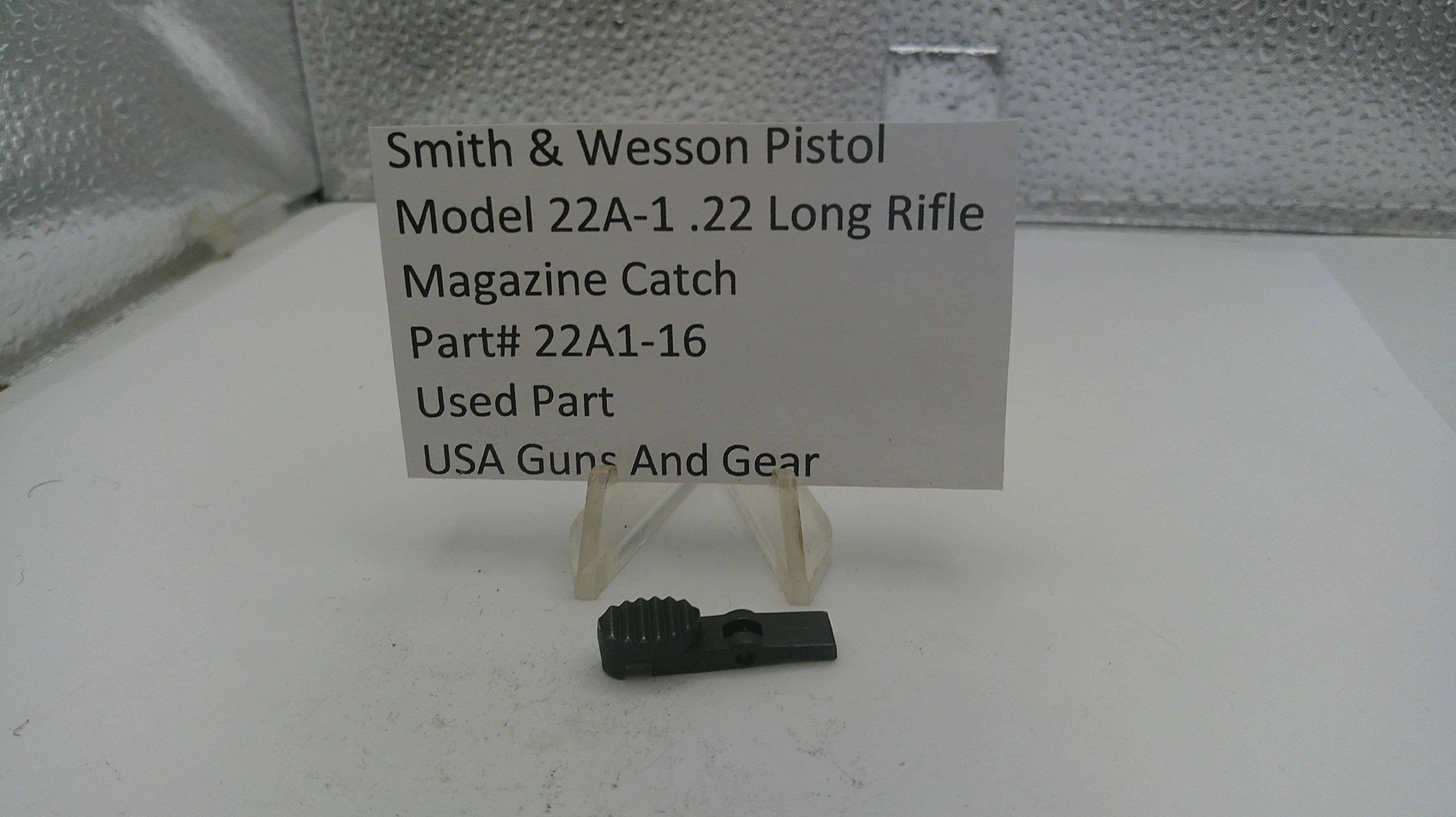 Smith & Wesson pistol magazine catch part with label on a white surface