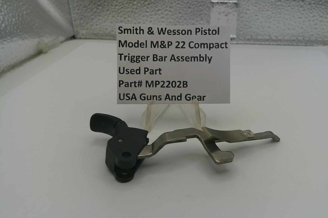 Smith & Wesson pistol trigger bar assembly on a white surface with a label.