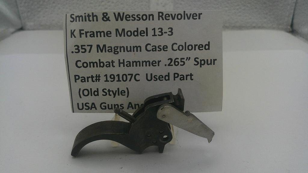 A used black metal Smith & Wesson revolver combat hammer part, displayed in front of a white paper label card with product details.