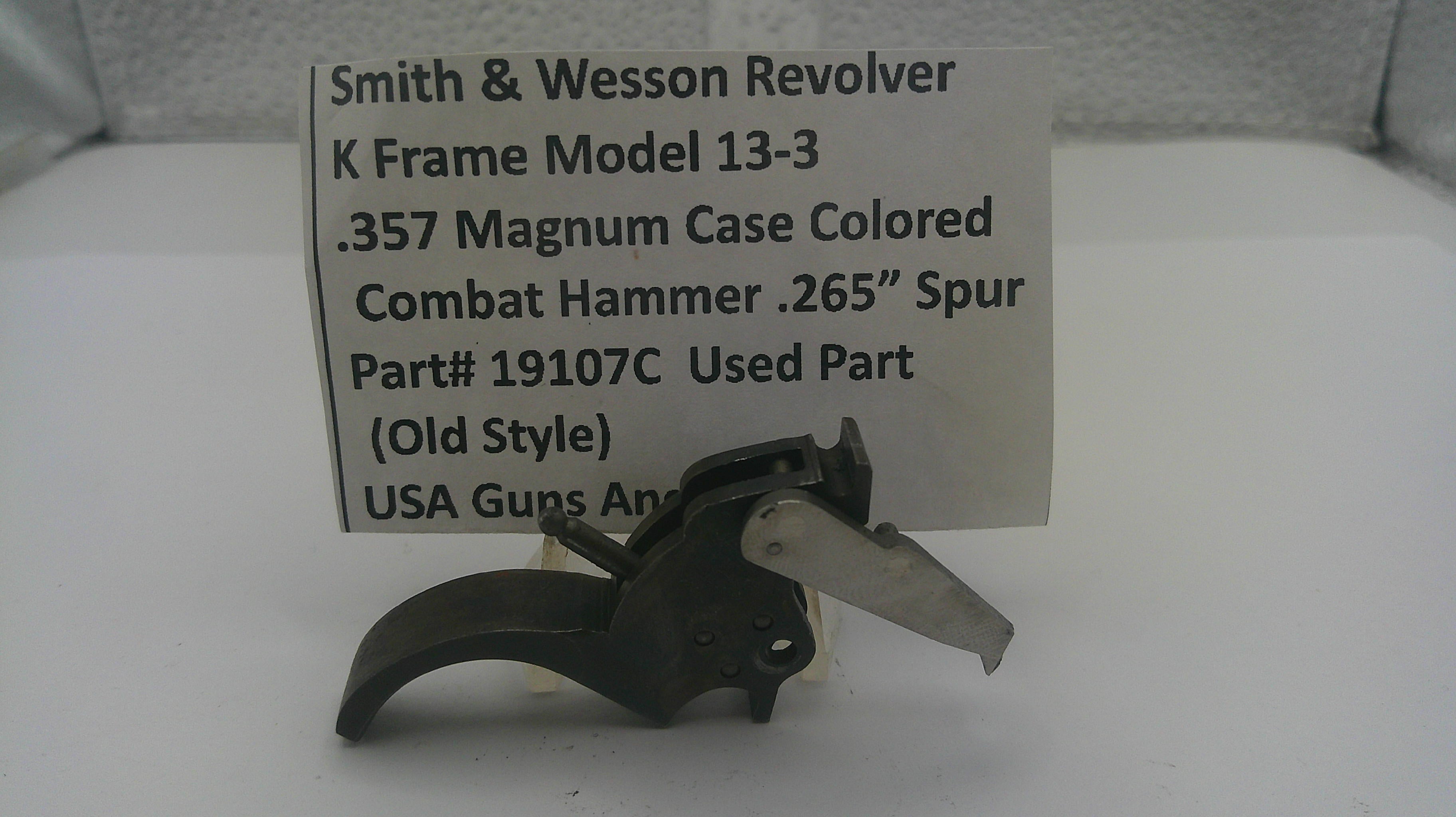 A used black metal Smith & Wesson revolver combat hammer part, displayed in front of a white paper label card with product details.