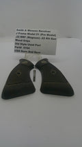 A pair of black textured revolver grip covers with a small metal pin and a white paper tag listing part details, photographed on a plain white background.