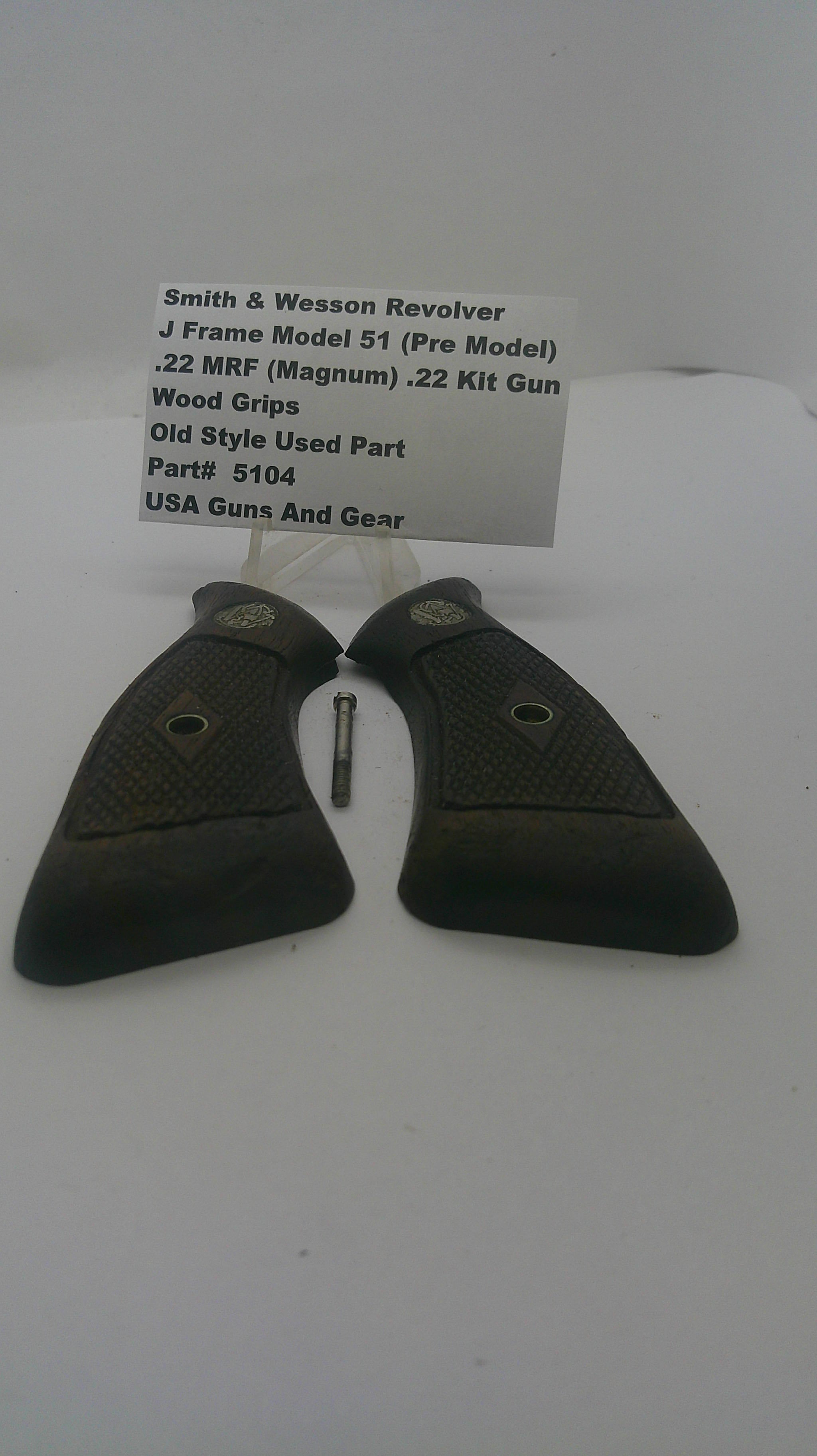 A pair of black textured revolver grip covers with a small metal pin and a white paper tag listing part details, photographed on a plain white background.