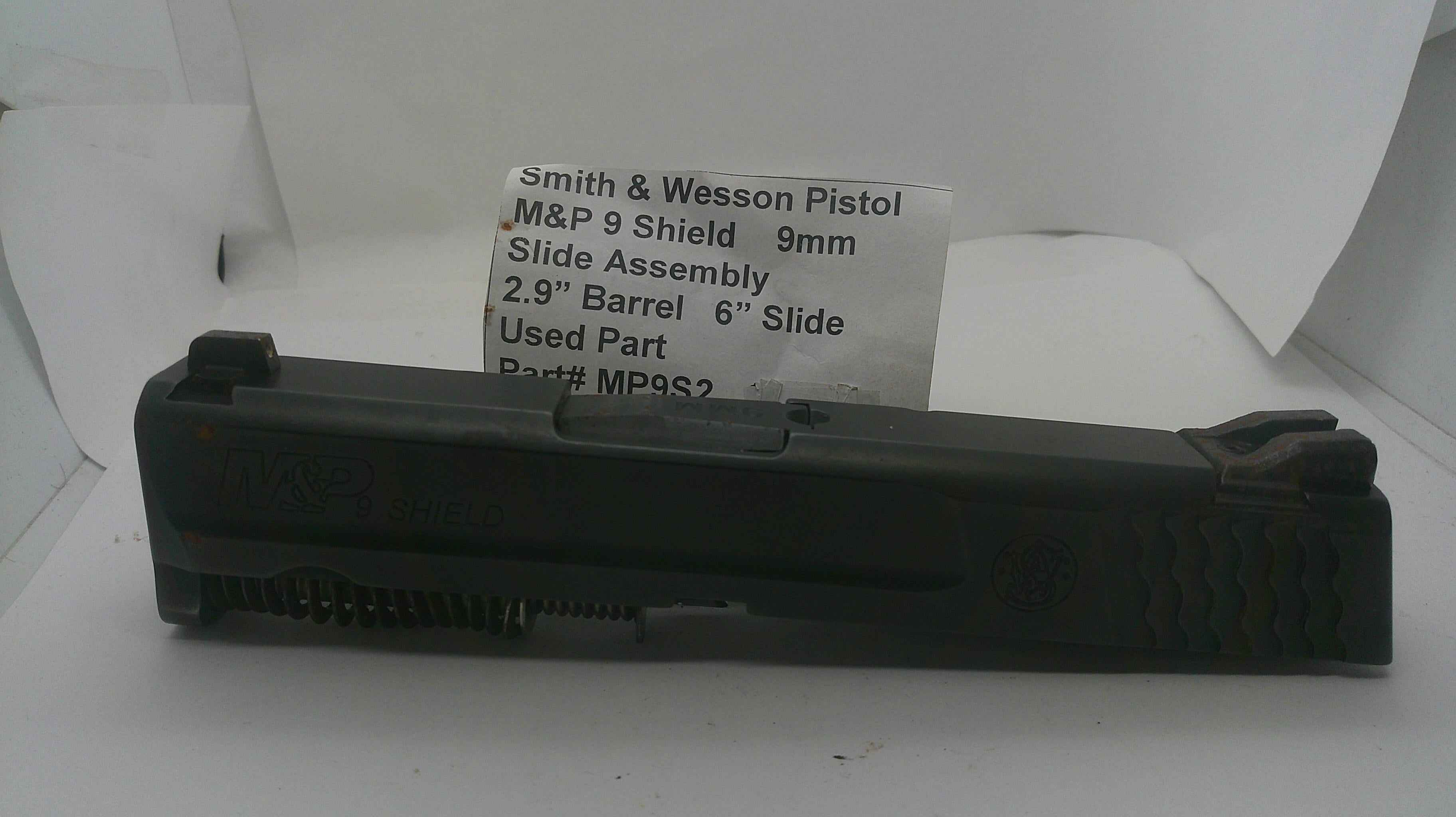 A used black Smith & Wesson pistol slide assembly, part number MP932, displayed on a white surface with a white paper label card behind it.