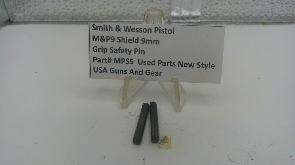 Two small black metal grip safety pins displayed on a clear plastic stand next to a white label card that reads 'Smith & Wesson Pistol M&P9 Shield 9mm Grip Safety Pin Part# MPS5 Used Parts New Style USA Guns And Gear'.