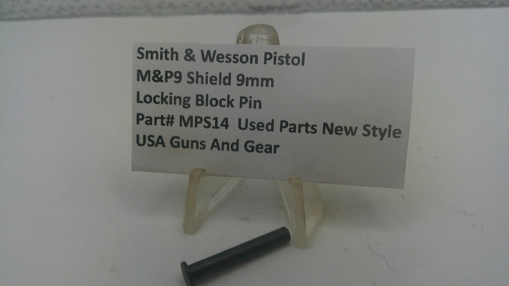 A small black metal locking block pin displayed on a clear plastic stand next to a white label card that reads 'Smith & Wesson Pistol M&P9 Shield 9mm Locking Block Pin Part# MPS14 Used Parts New Style USA Guns And Gear' on a white surface.