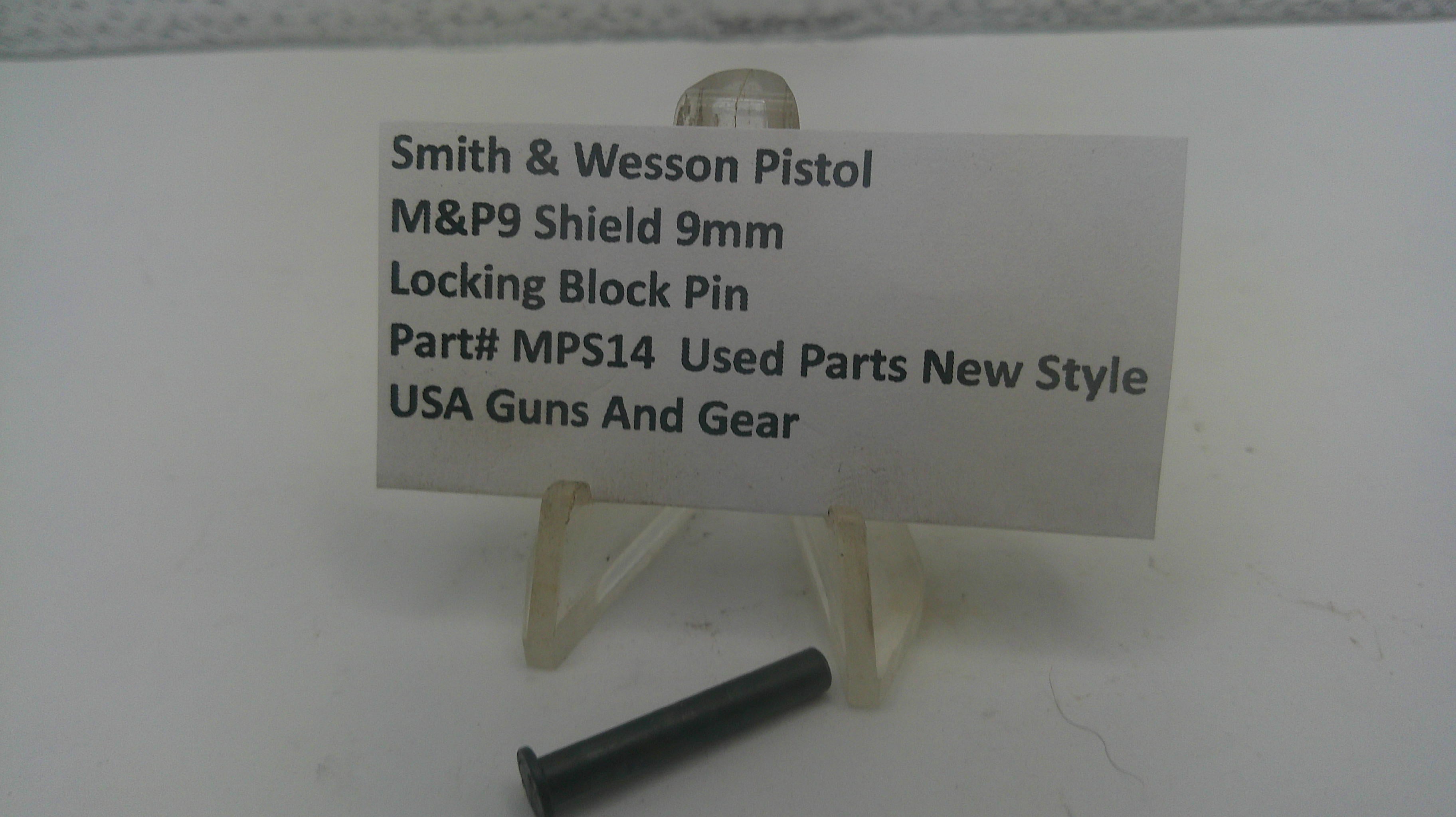 A small black metal locking block pin displayed on a clear plastic stand next to a white label card that reads 'Smith & Wesson Pistol M&P9 Shield 9mm Locking Block Pin Part# MPS14 Used Parts New Style USA Guns And Gear' on a white surface.