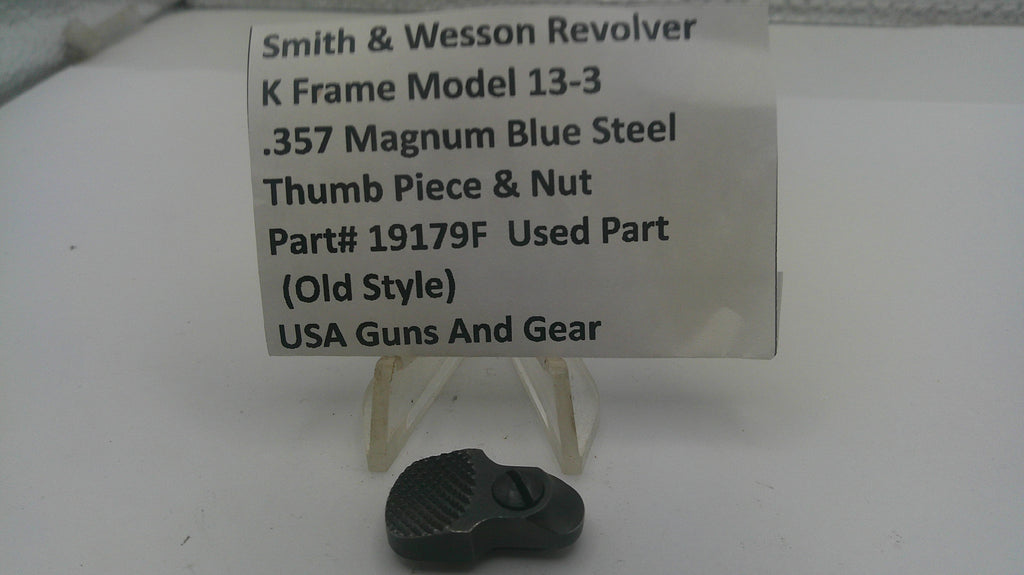 A small black metal thumb piece and nut part for a Smith & Wesson revolver, displayed below a white label card on a white surface.
