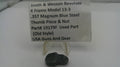 A small black metal thumb piece and nut part for a Smith & Wesson revolver, displayed below a white label card on a white surface.