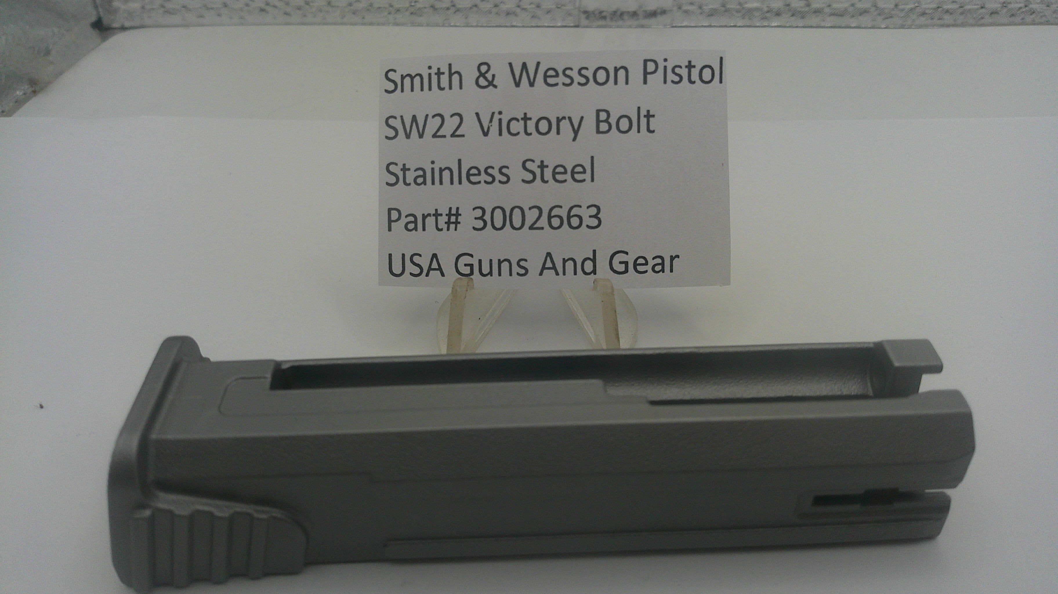 A dark gray metal receiver or grip component for a Smith & Wesson pistol, displayed on a white surface with a paper label card behind it reading 'Smith & Wesson Pistol SW22 Victory Bolt Stainless Steel Part# 3002663 USA Guns And Gear'.