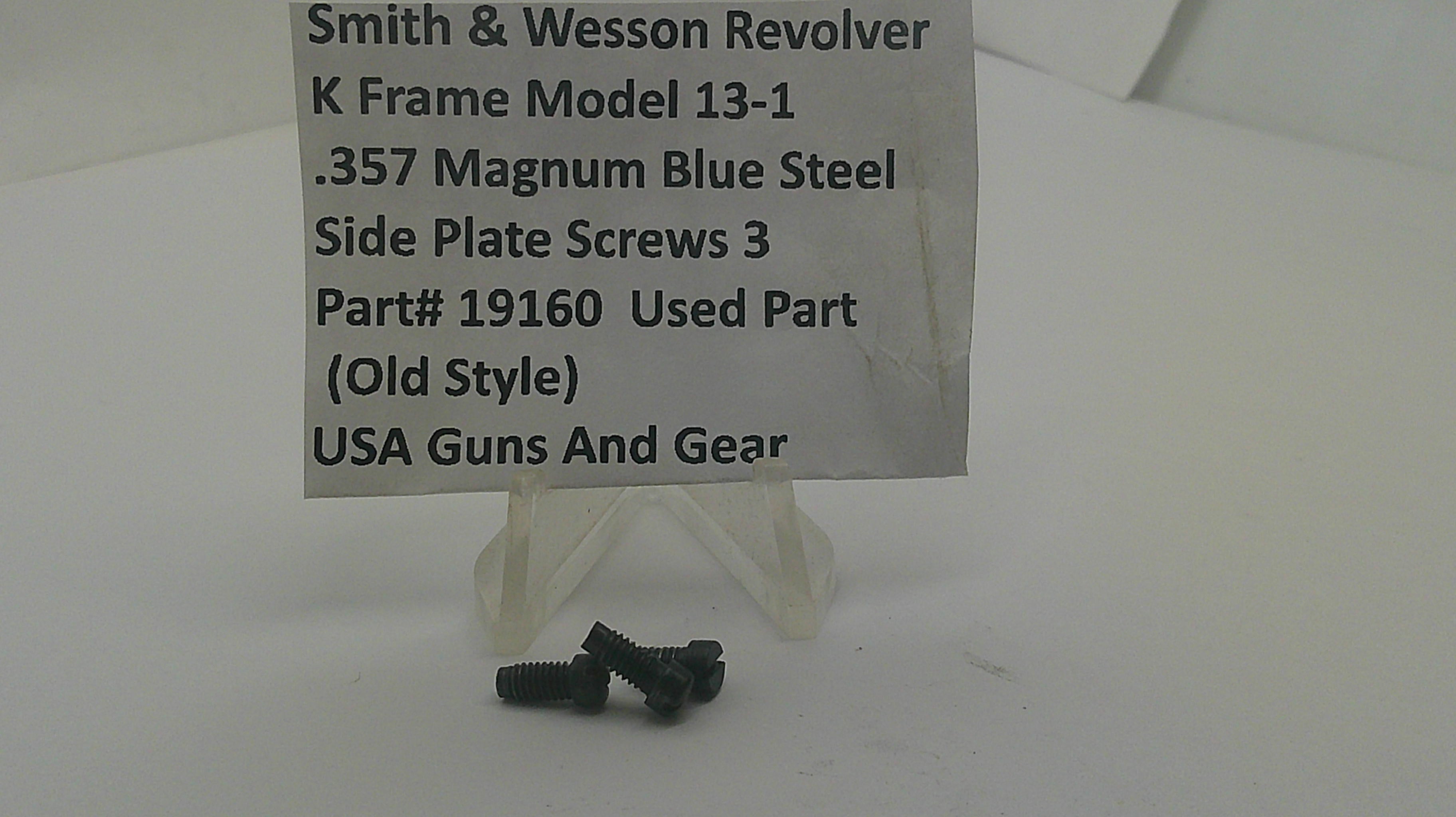 Three small black metal screws displayed on a clear plastic stand in front of a white sign that reads 'Smith & Wesson Revolver K Frame Model 13-1 .357 Magnum Blue Steel Side Plate Screws 3 Part# 19160 Used Part USA Guns And Gear'.