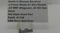 A small metal used part for a Smith & Wesson revolver, displayed on a clear plastic stand in front of a white sign with product details.