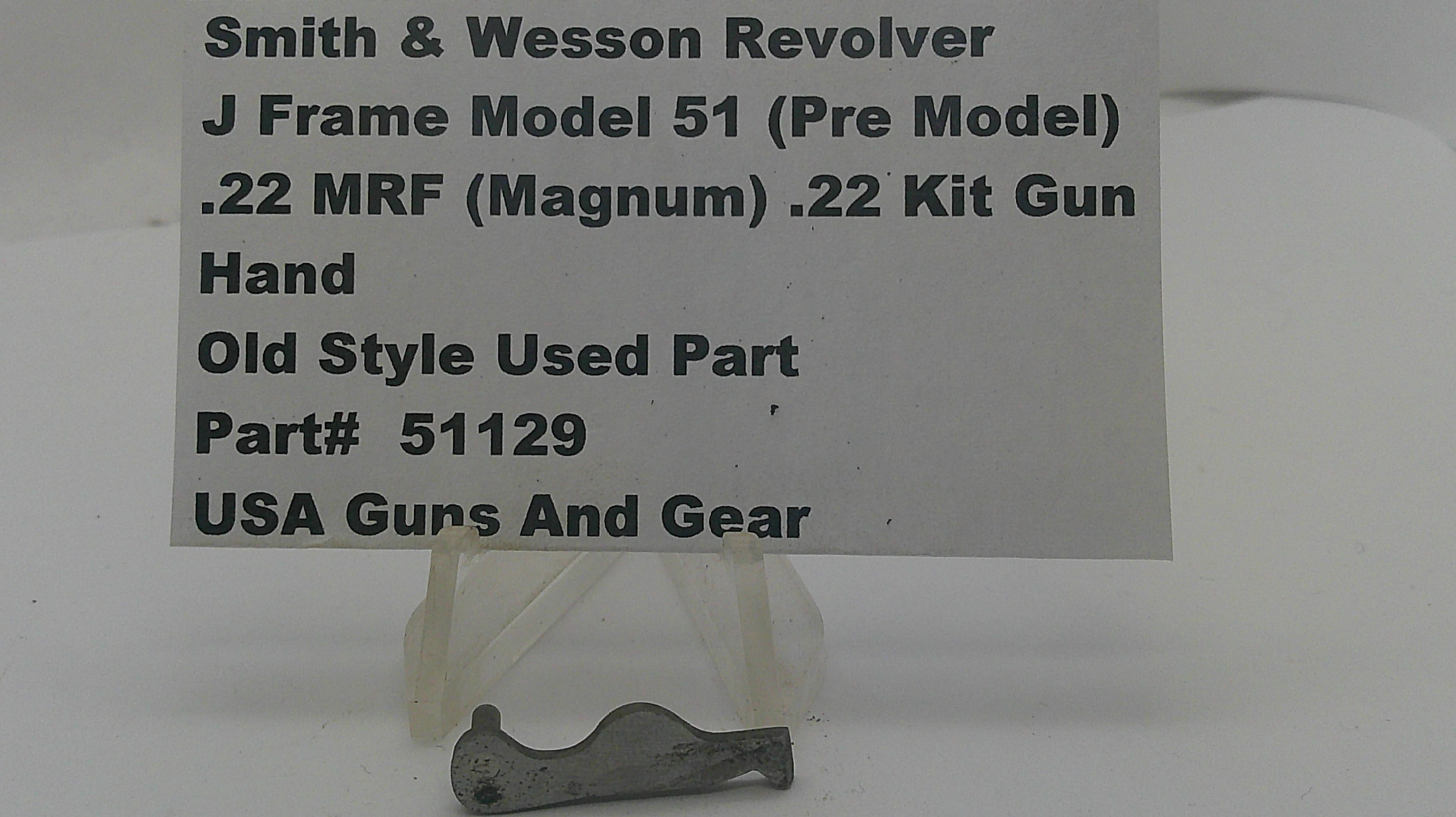 A small metal used part for a Smith & Wesson revolver, displayed on a clear plastic stand in front of a white sign with product details.