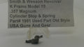 A small metal cylinder stop and spring part displayed on a clear plastic stand, with a paper label reading 'Smith & Wesson Revolver K Frame Model 19 .357 Magnum Cylinder Stop & Spring Part# 1981 Used Part Old Style USA Guns And Gear' in the background.