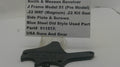 A used black metal side plate and screws part for a Smith & Wesson revolver, displayed on a white surface with a white label card showing the part details.