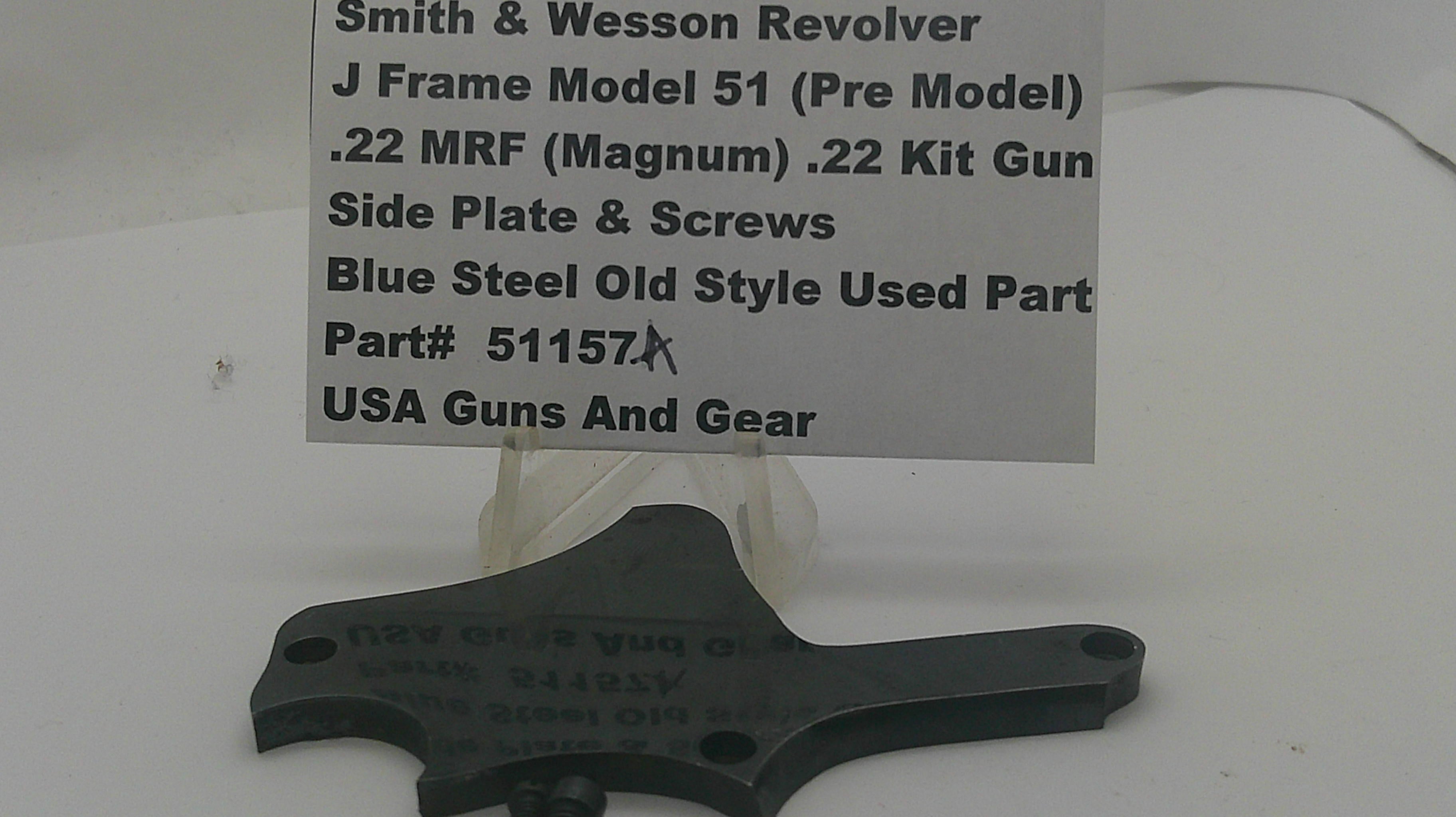 A used black metal side plate and screws part for a Smith & Wesson revolver, displayed on a white surface with a white label card showing the part details.