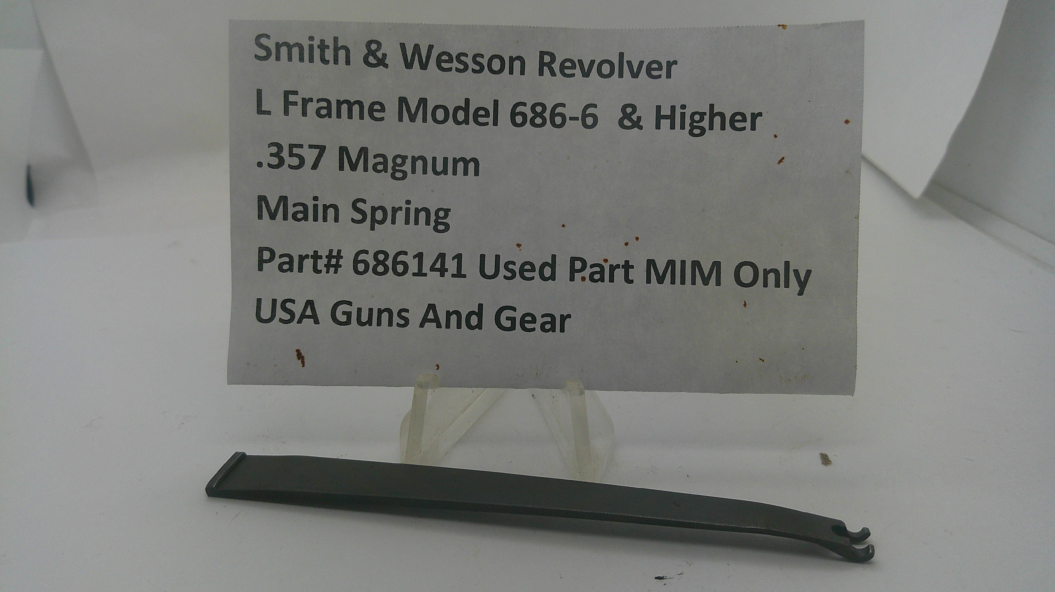 A used black metal main spring for a Smith & Wesson revolver, displayed on a clear plastic stand with a white paper label showing the part number and model details.