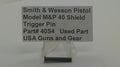 A small black metal trigger pin displayed below a gray sign that reads 'Smith & Wesson Pistol Model M&P 40 Shield Trigger Pin Part# 40S4 Used Part USA Guns and Gear' on a plain light background.
