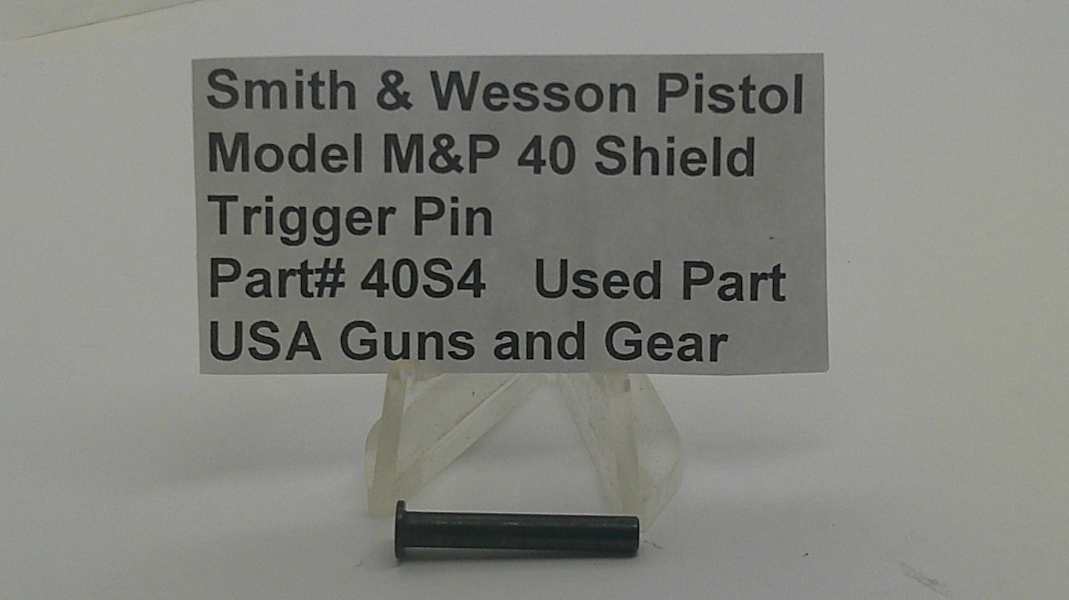 A small black metal trigger pin displayed below a gray sign that reads 'Smith & Wesson Pistol Model M&P 40 Shield Trigger Pin Part# 40S4 Used Part USA Guns and Gear' on a plain light background.