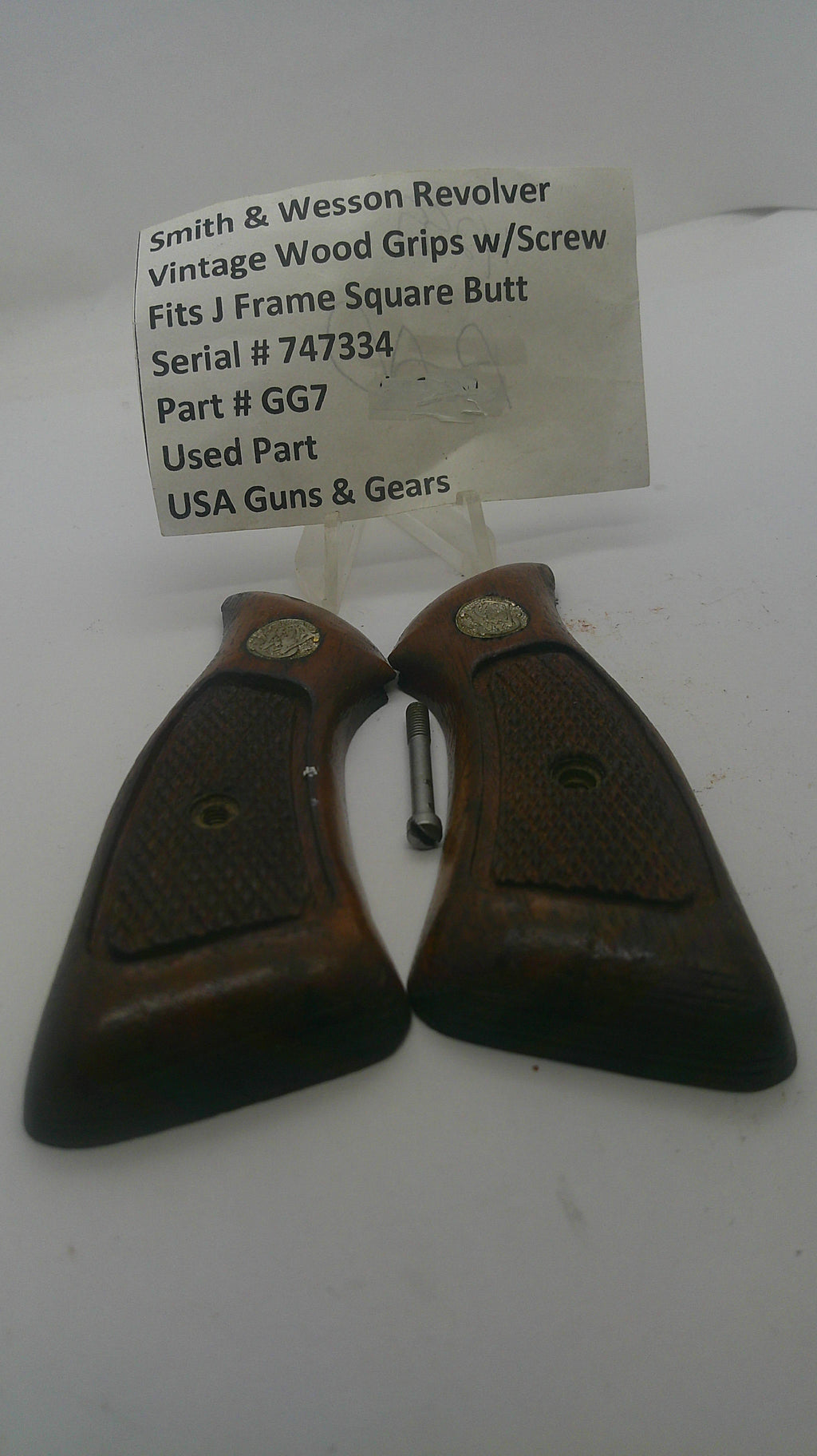 A pair of vintage wooden gun grips with a small metal pin and a white paper tag showing part details, photographed on a white background.