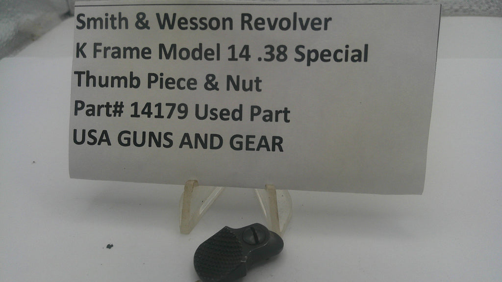 A used black metal Smith & Wesson revolver thumb piece and nut part, displayed on a small clear stand in front of a white sign with black text identifying it as a used part.