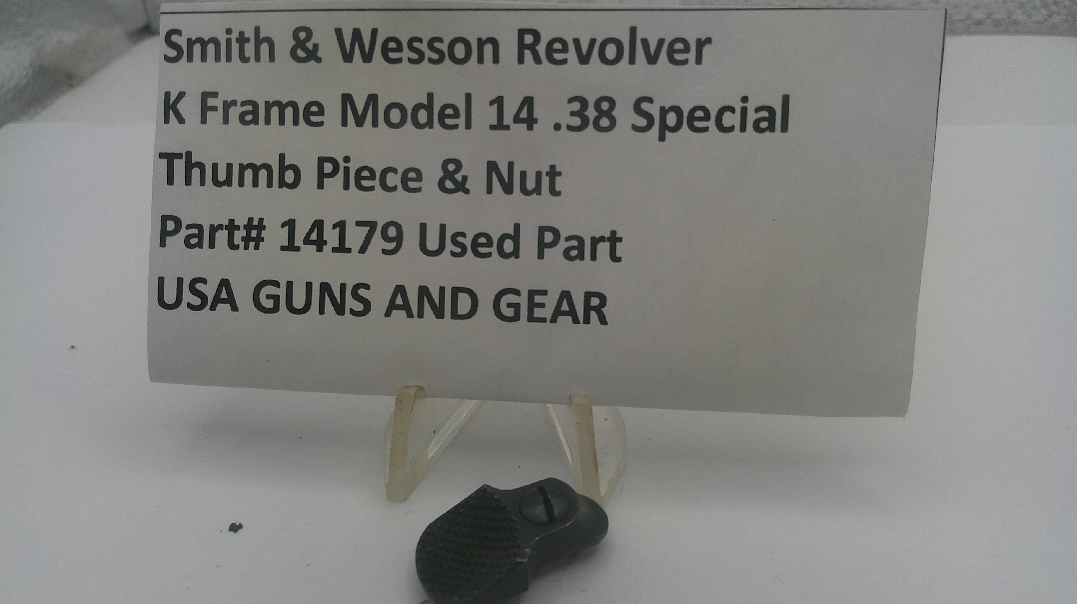 A used black metal Smith & Wesson revolver thumb piece and nut part, displayed on a small clear stand in front of a white sign with black text identifying it as a used part.
