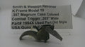 A used metal Smith & Wesson revolver trigger component, model K Frame Model 19, shown in front of a white paper label with product details.