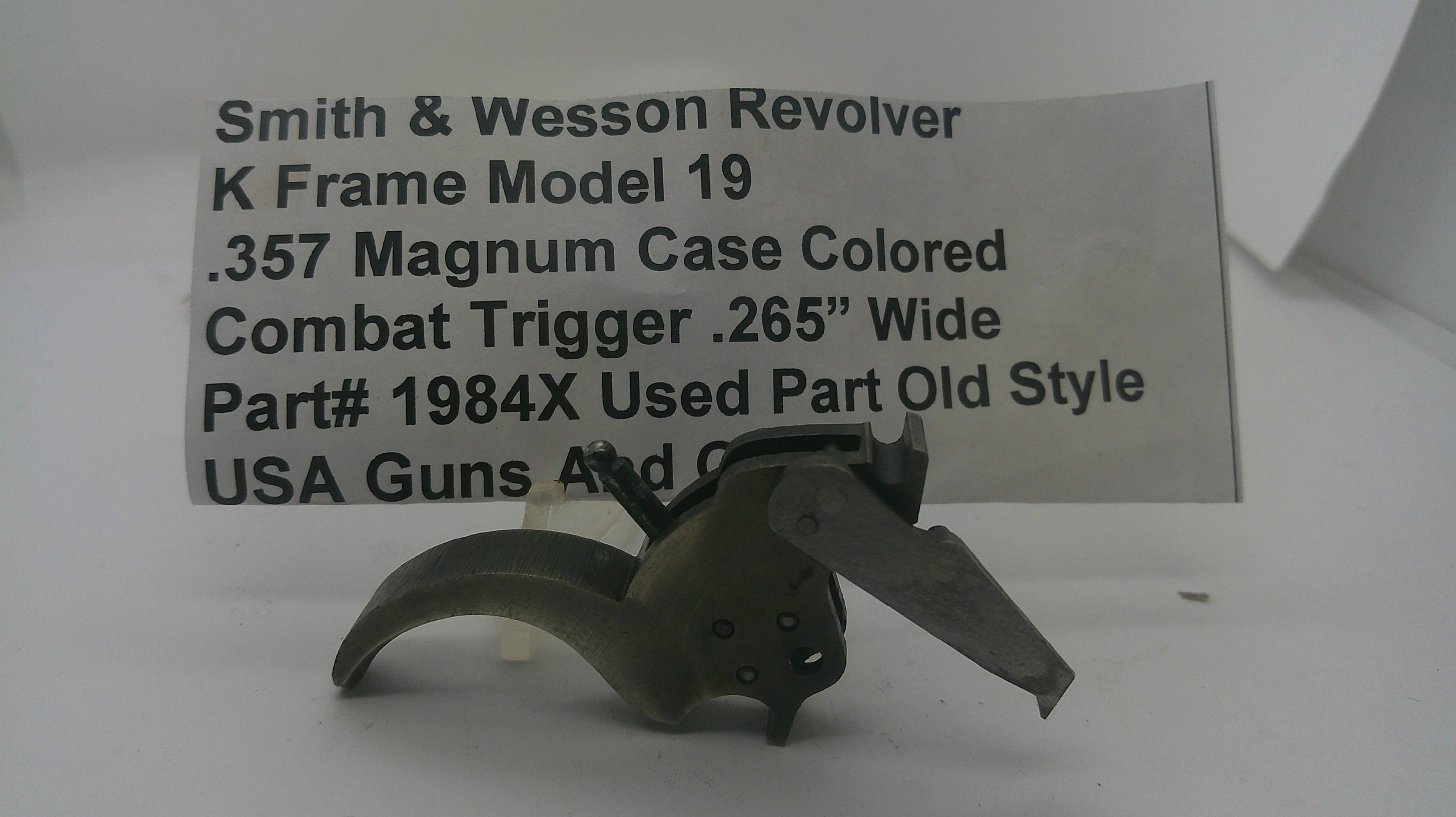 A used metal Smith & Wesson revolver trigger component, model K Frame Model 19, shown in front of a white paper label with product details.