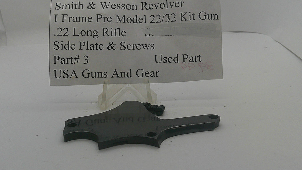 A used black metal side plate and screws kit for a Smith & Wesson revolver, displayed on a clear plastic stand with a paper label card. The label reads 'Smith & Wesson Revolver I Frame Pre Model 22/32 Kit Gun .