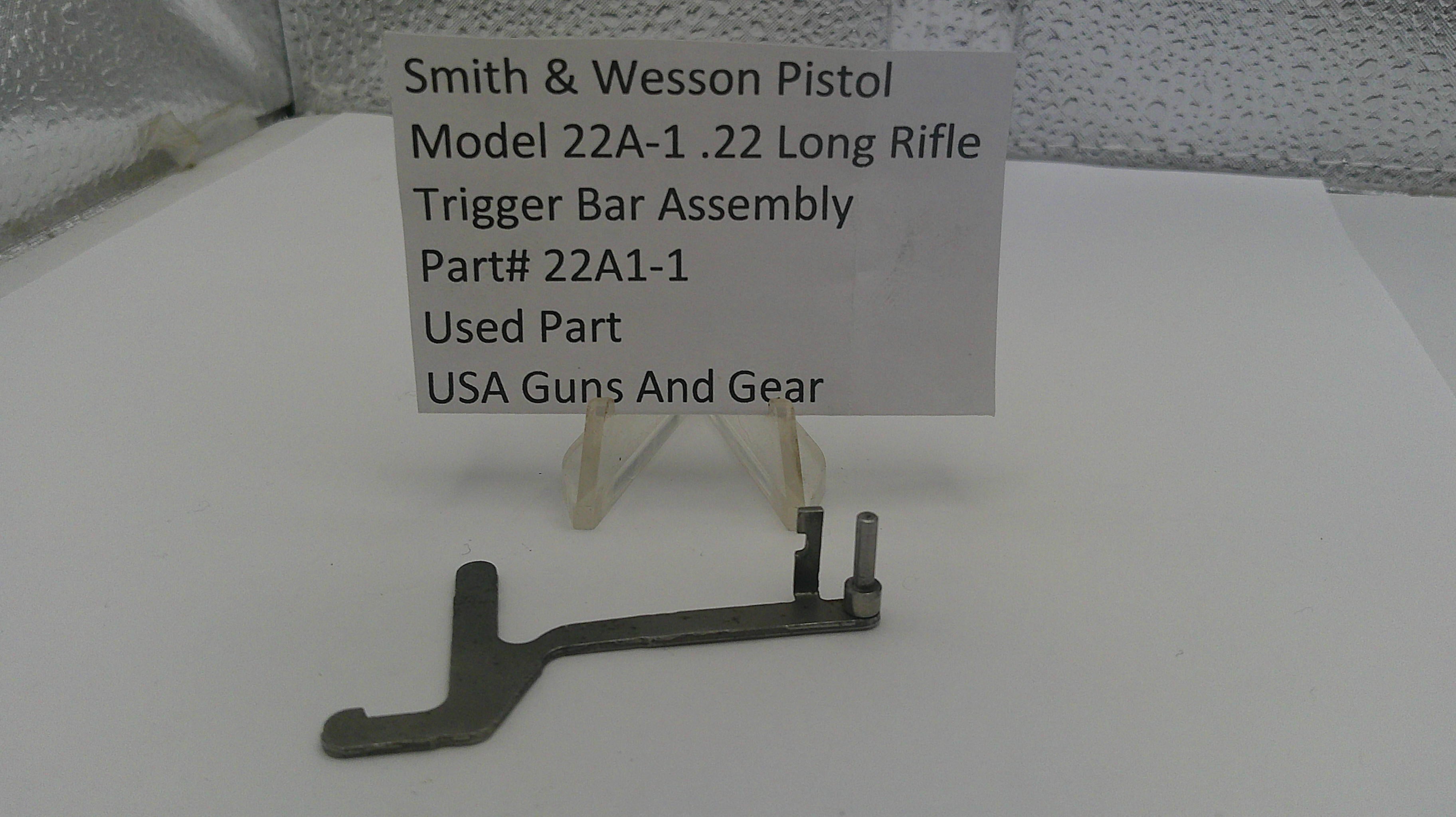 Smith & Wesson pistol trigger bar assembly on a white surface with a label.