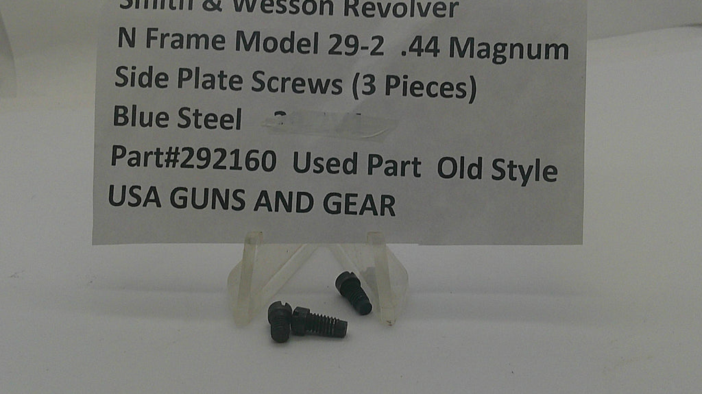 Three small dark steel screws displayed on a clear plastic stand in front of a white sign that reads 'Smith & Wesson Revolver N Frame Model 29-2 .44 Magnum Side Plate Screws (3 Pieces) Blue Steel Part#292160 Used Part Old Style USA GUNS AND GEAR'.