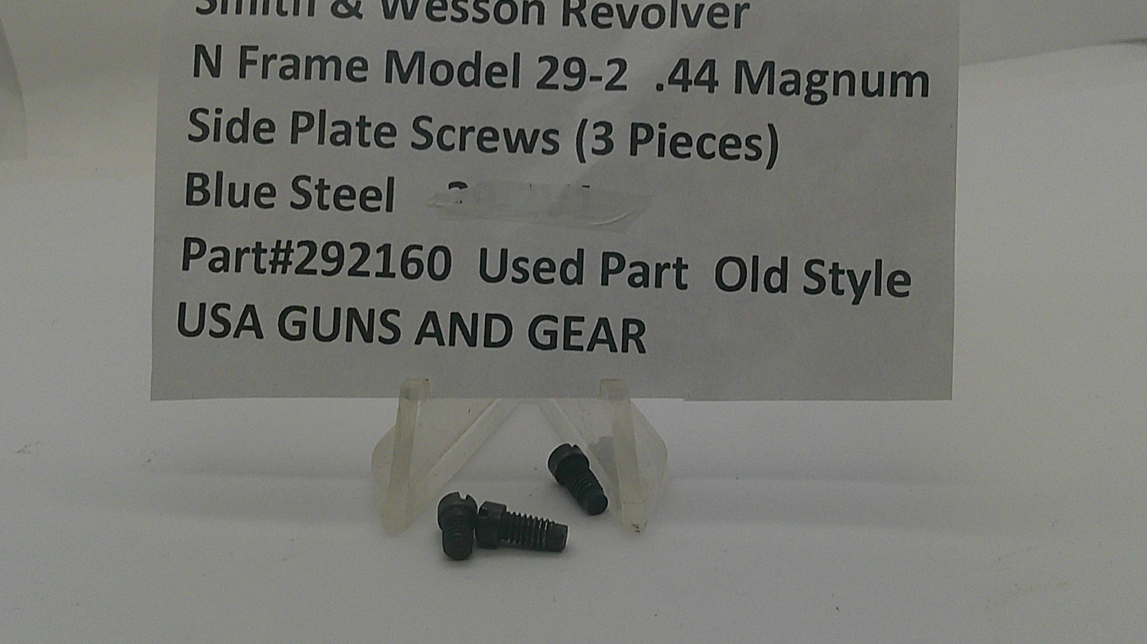 Three small dark steel screws displayed on a clear plastic stand in front of a white sign that reads 'Smith & Wesson Revolver N Frame Model 29-2 .44 Magnum Side Plate Screws (3 Pieces) Blue Steel Part#292160 Used Part Old Style USA GUNS AND GEAR'.