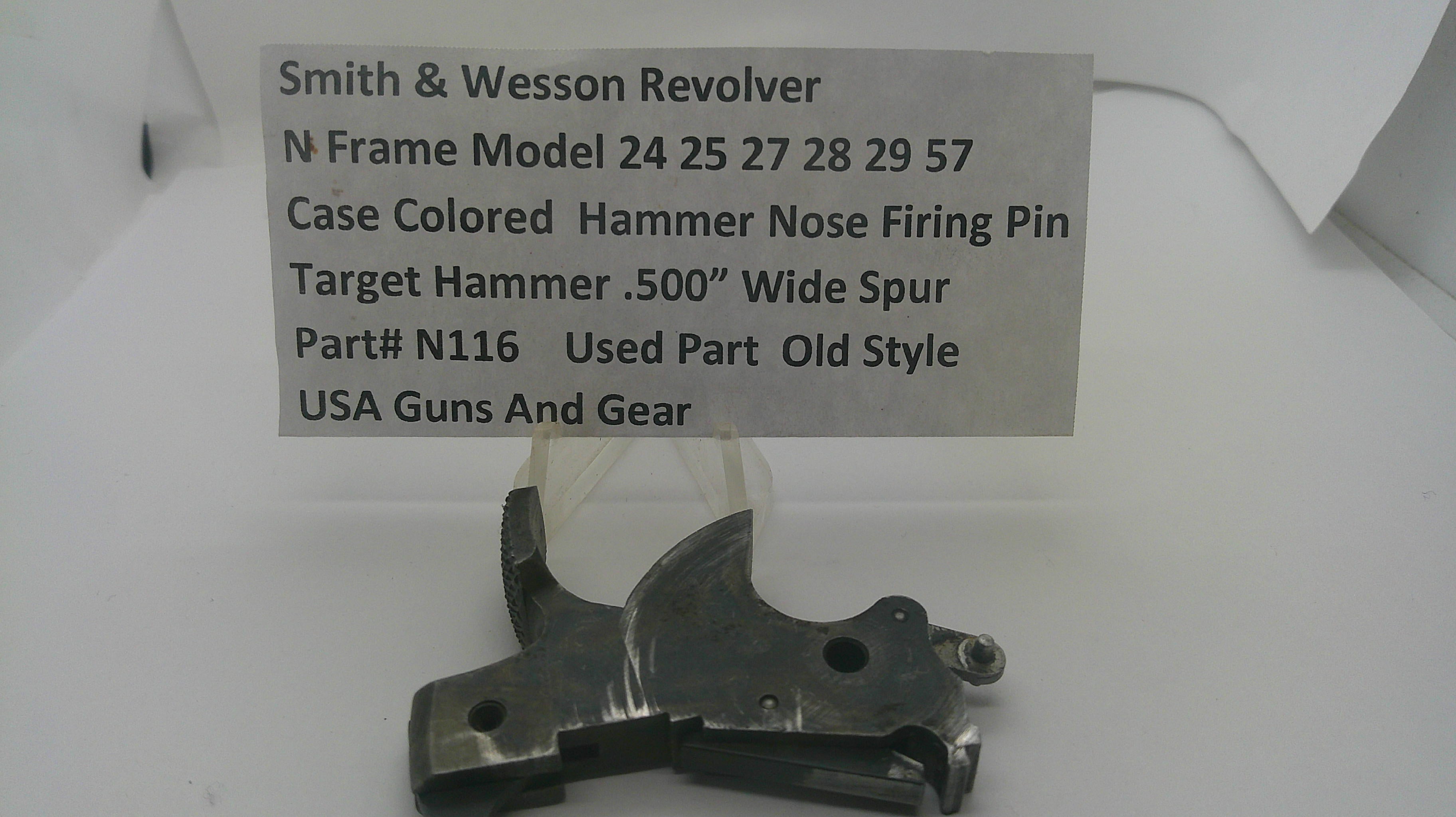 A used metal hammer nose part for a Smith & Wesson revolver, displayed on a white surface with a handwritten label card above it.