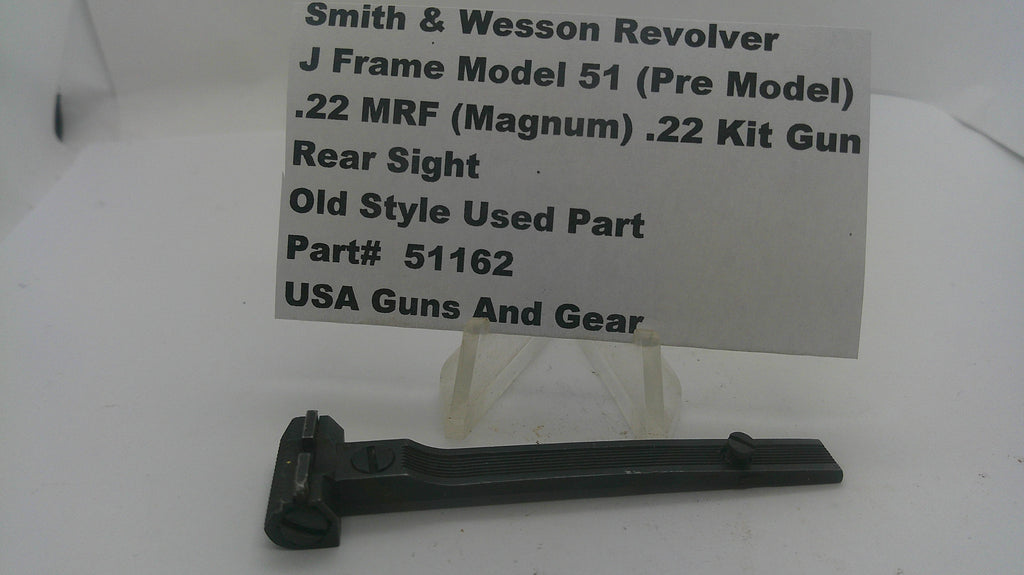 A black metal Smith & Wesson revolver rear sight part displayed on a clear stand in front of a white paper label card with printed specifications.