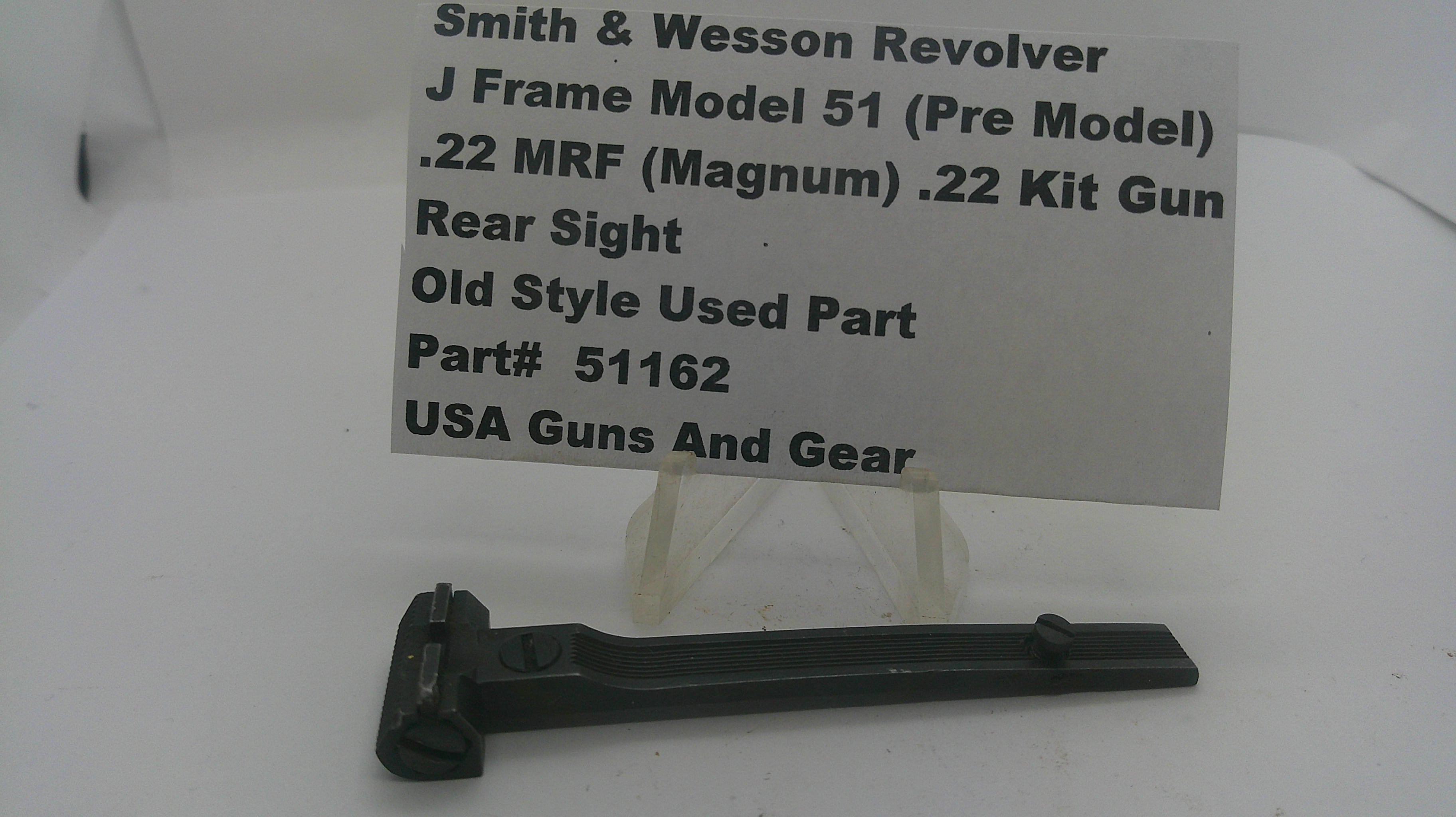 A black metal Smith & Wesson revolver rear sight part displayed on a clear stand in front of a white paper label card with printed specifications.
