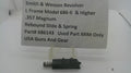 A used black metal Smith & Wesson revolver rebound slide and spring part, displayed on a clear plastic stand with a white paper label card in the background.