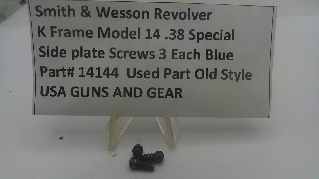 Three small black metal screws displayed on a clear plastic stand in front of a white sign that reads 'Smith & Wesson Revolver K Frame Model 14 .38 Special Side plate Screws 3 Each Blue Part# 14144 Used Part Old Style USA GUNS AND GEAR'.
