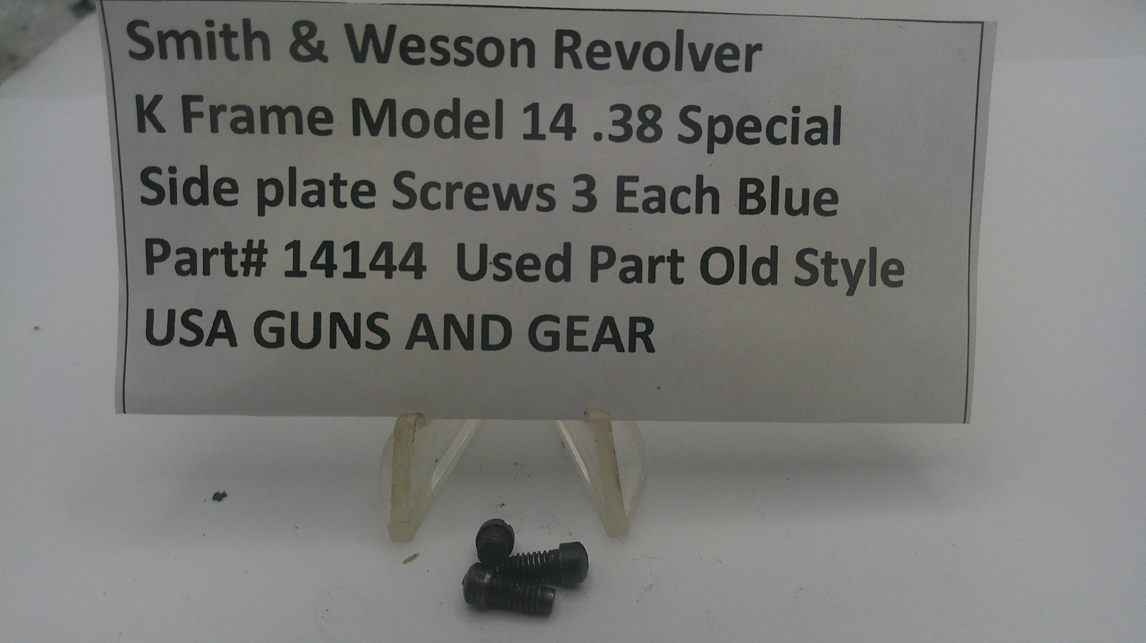 Three small black metal screws displayed on a clear plastic stand in front of a white sign that reads 'Smith & Wesson Revolver K Frame Model 14 .38 Special Side plate Screws 3 Each Blue Part# 14144 Used Part Old Style USA GUNS AND GEAR'.