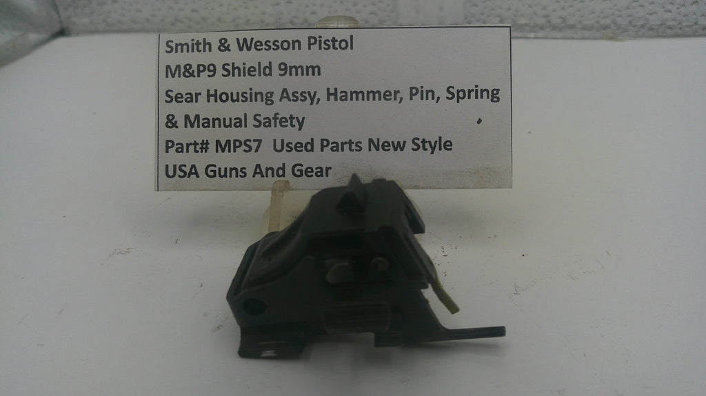 A used black metal Smith & Wesson pistol safety switch assembly with a small white paper label showing part details, photographed on a white surface.