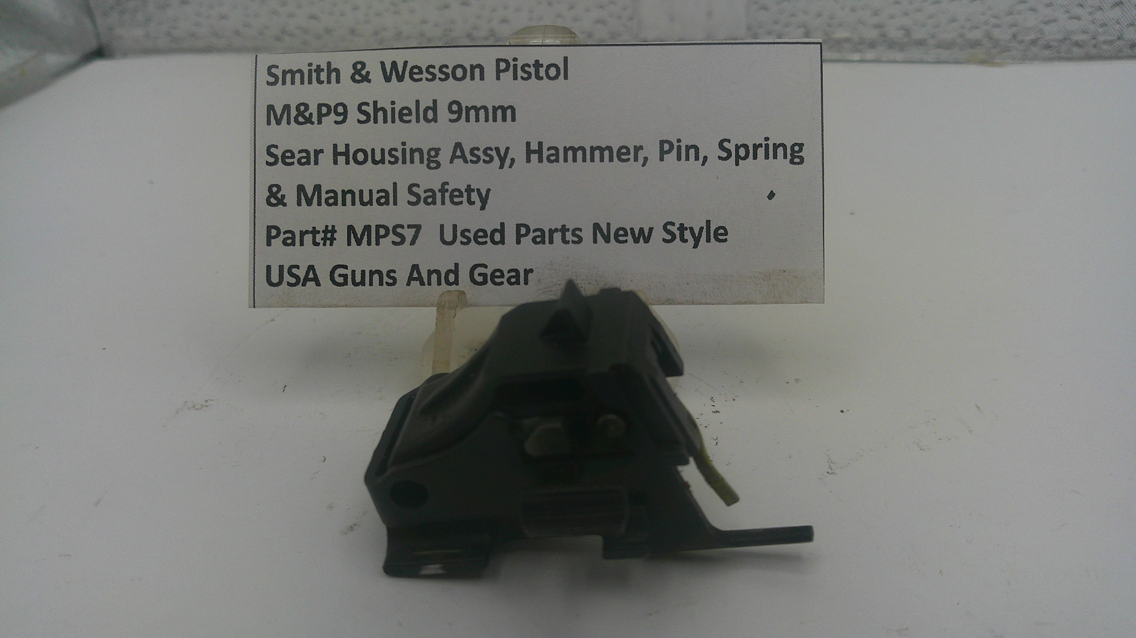 A used black metal Smith & Wesson pistol safety switch assembly with a small white paper label showing part details, photographed on a white surface.
