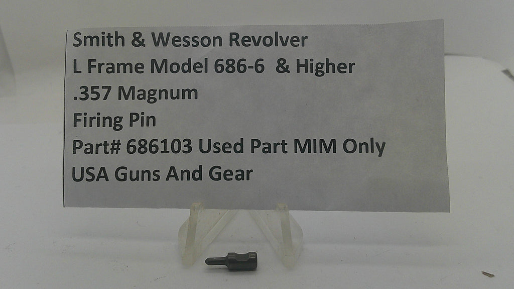 A small metal firearm firing pin part displayed on a clear plastic stand, with a paper label reading 'Smith & Wesson Revolver L Frame Model 686-6 & Higher .357 Magnum Firing Pin Part# 686103 Used Part MIM Only USA Guns And Gear'.