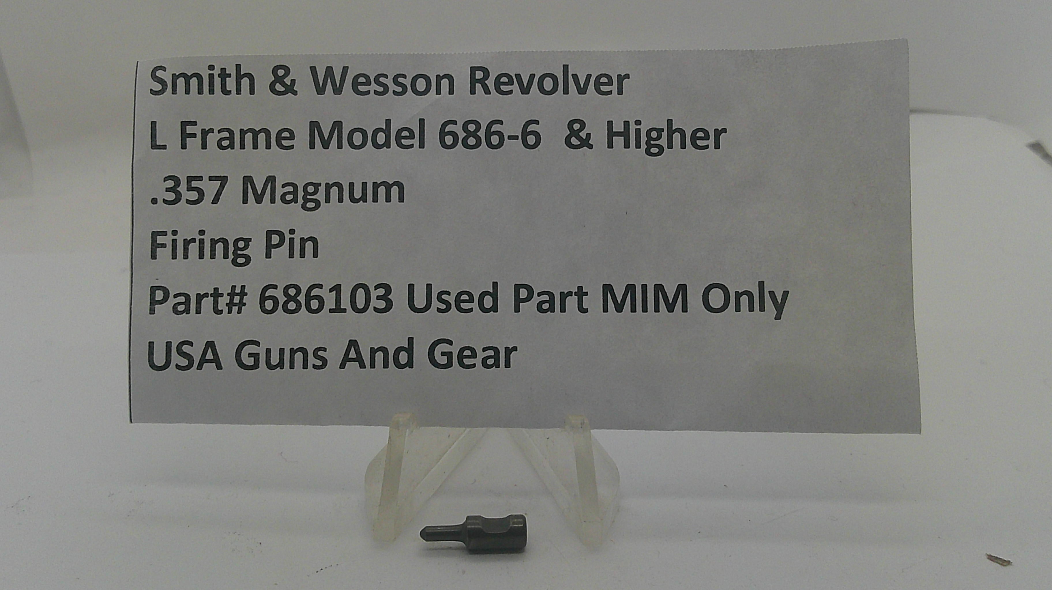 A small metal firearm firing pin part displayed on a clear plastic stand, with a paper label reading 'Smith & Wesson Revolver L Frame Model 686-6 & Higher .357 Magnum Firing Pin Part# 686103 Used Part MIM Only USA Guns And Gear'.