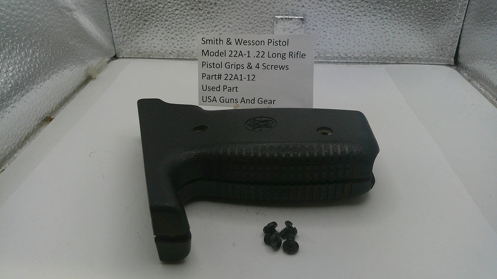 Black pistol grip and screws on a white surface with a label in the background.