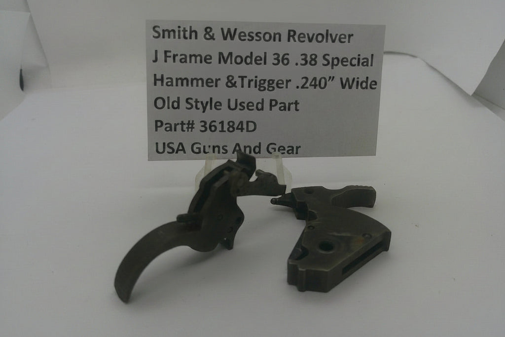 A used metal hammer and trigger assembly for a Smith & Wesson revolver, displayed on a white surface with a paper label card showing the part details.