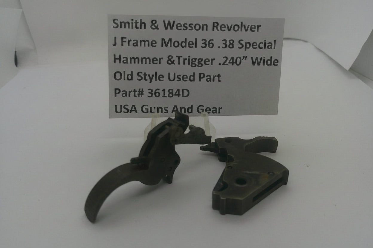 A used metal hammer and trigger assembly for a Smith & Wesson revolver, displayed on a white surface with a paper label card showing the part details.